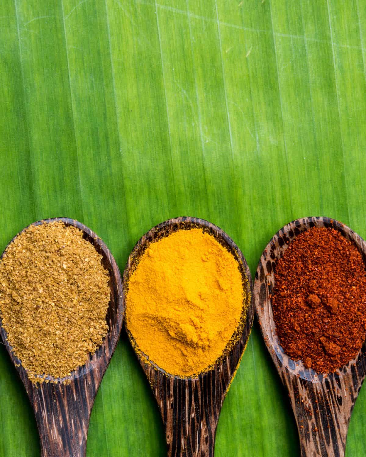 Cumin powder, turmeric powder and chilli powder on wooden spoons.