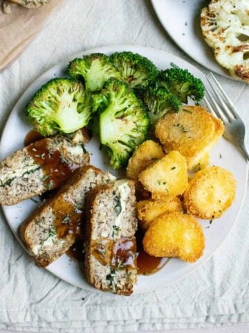 A plate of food with a nut roast, potatoes and broccoli.
