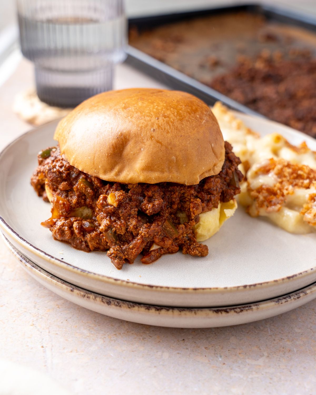 Vegan sloppy joes in a burger bun on a plate with mac and cheese.
