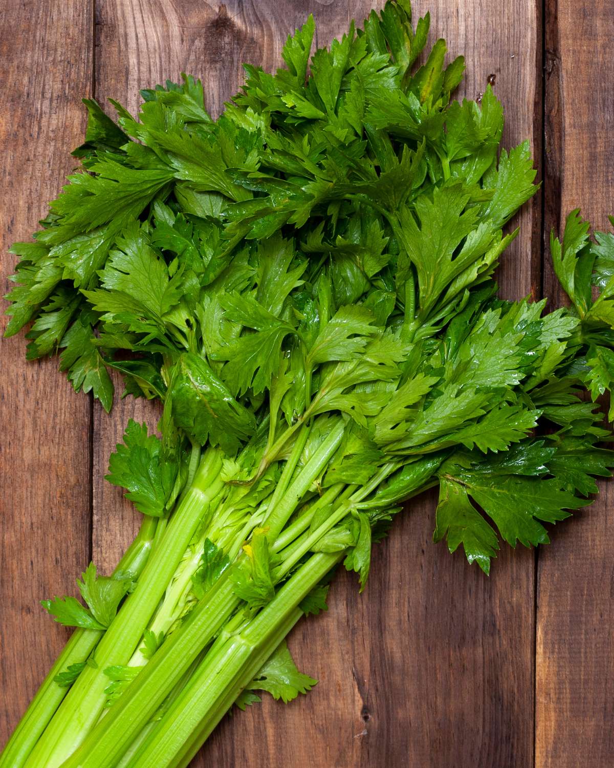 Celery stalks with celery leaves on a wooden table.