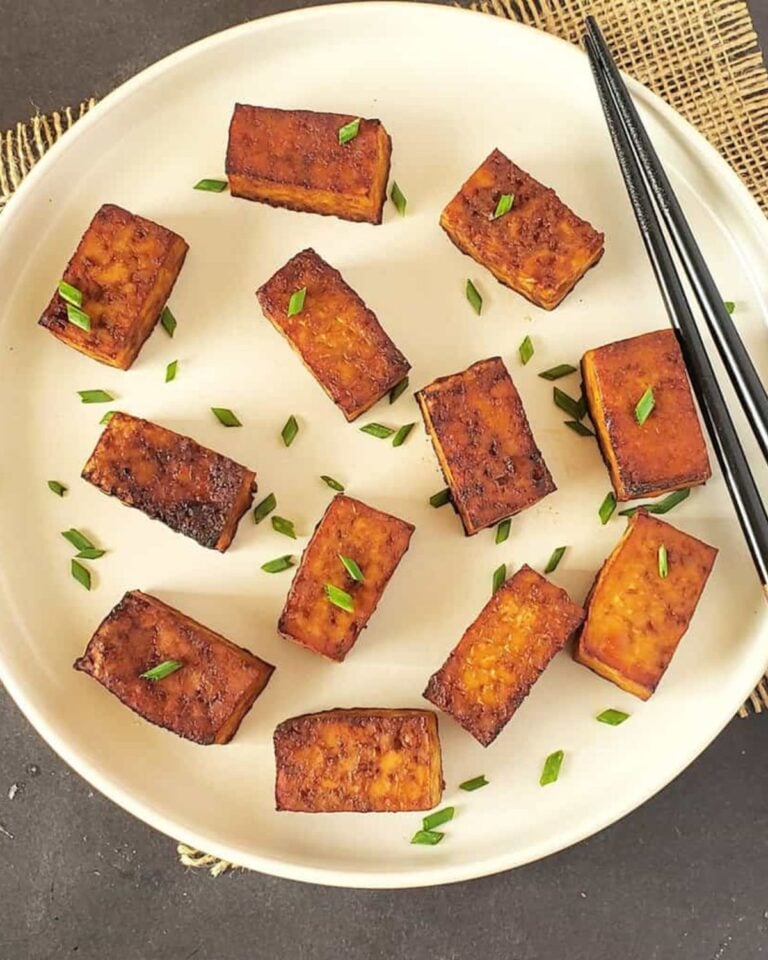 Pieces of smoked tofu on a plate topped with spring onions.