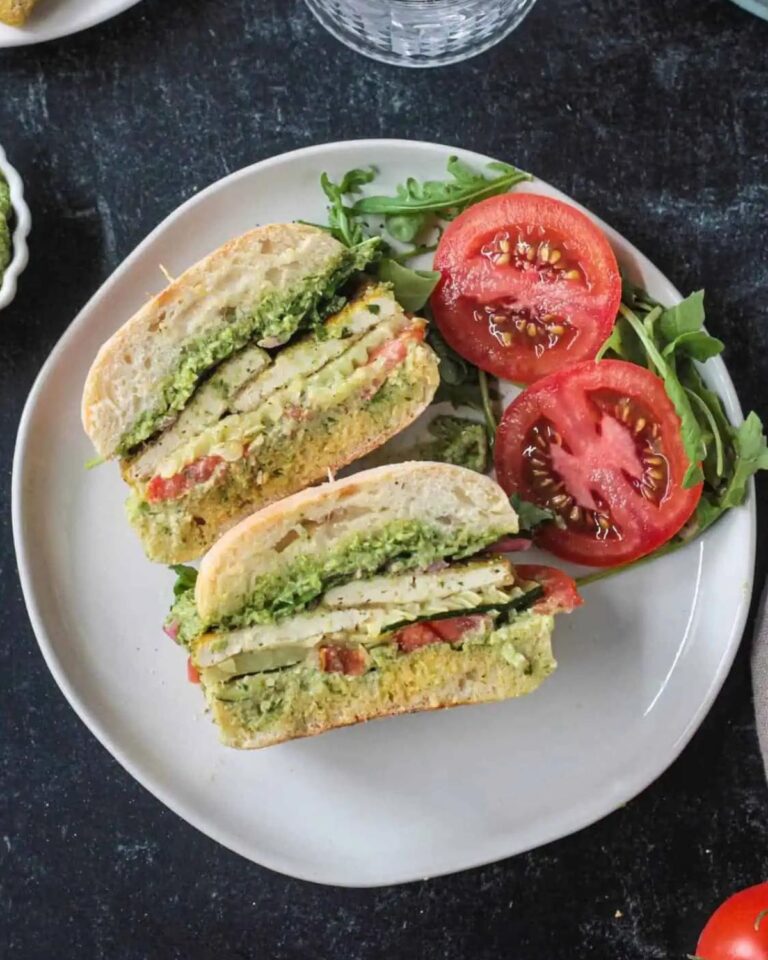 Tofu pesto sandwich with slices of tomato on the side.